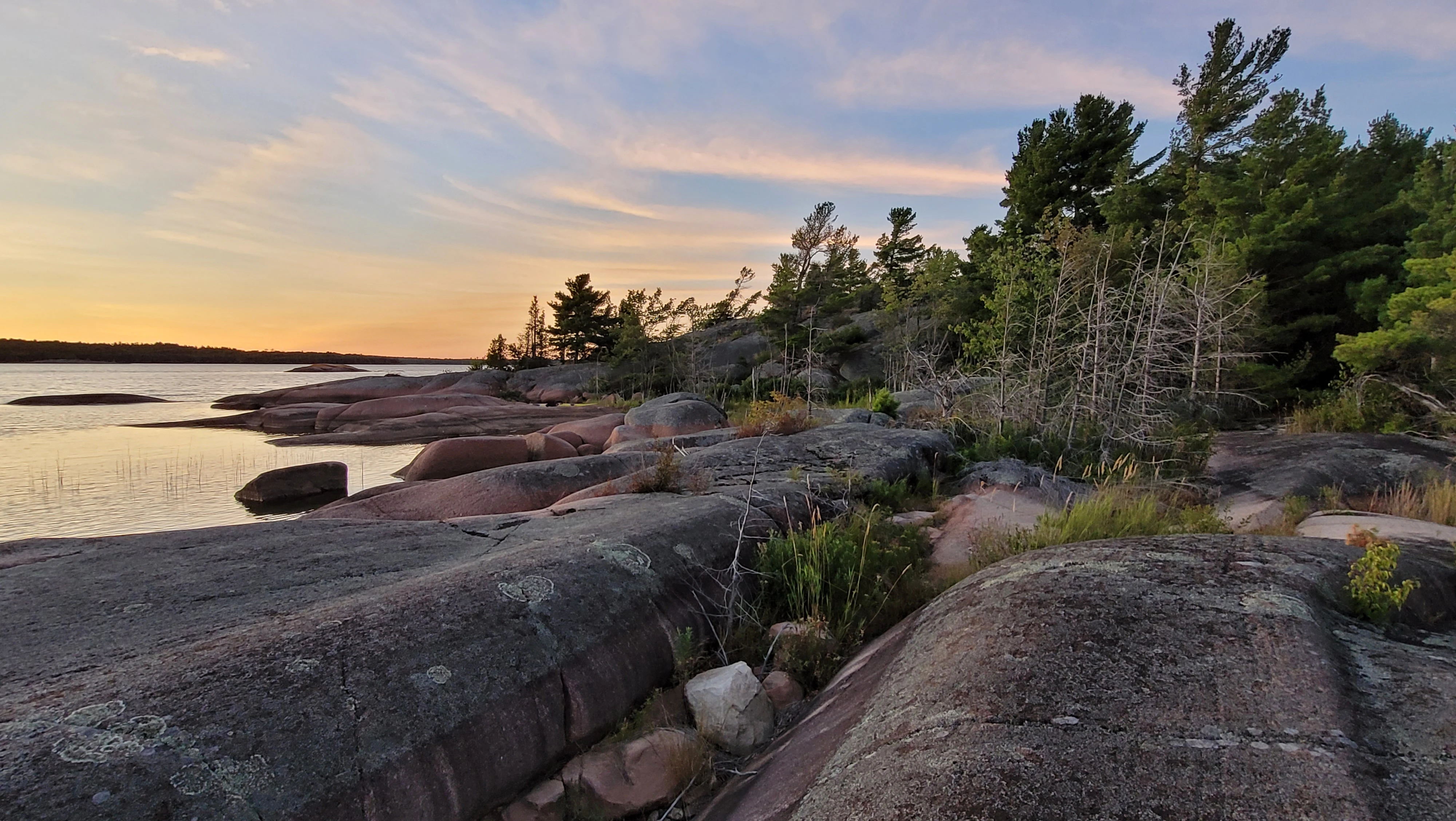 A sunset sky over smooth red granite rocks and pine trees on North Benjamin Island in the North Channel of Lake Huron in Ontario, Canada