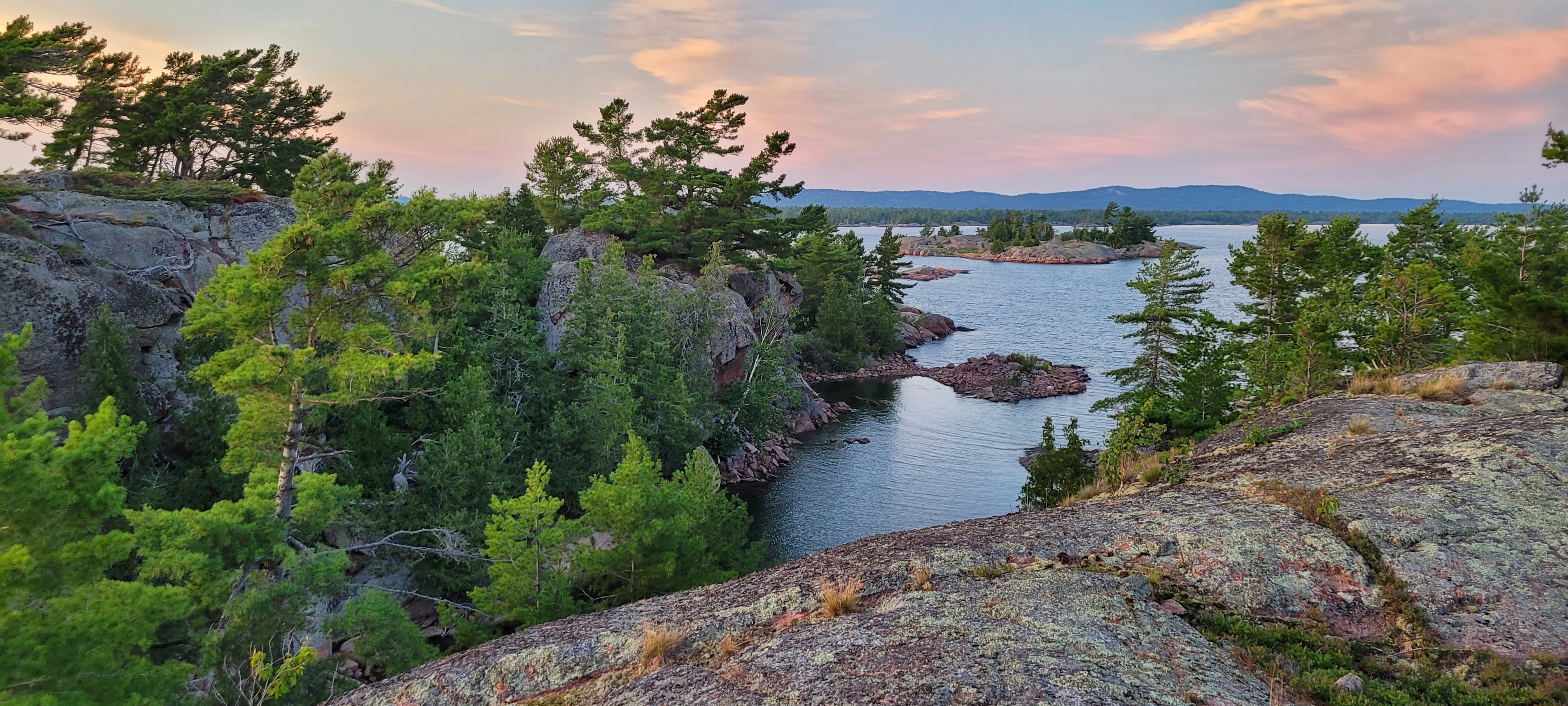 A vista on top of a cliff overlooking another cliff covered with trees and the open Great Lakes in the background on North Benjamin Islands in Lake Huron's North Channel.