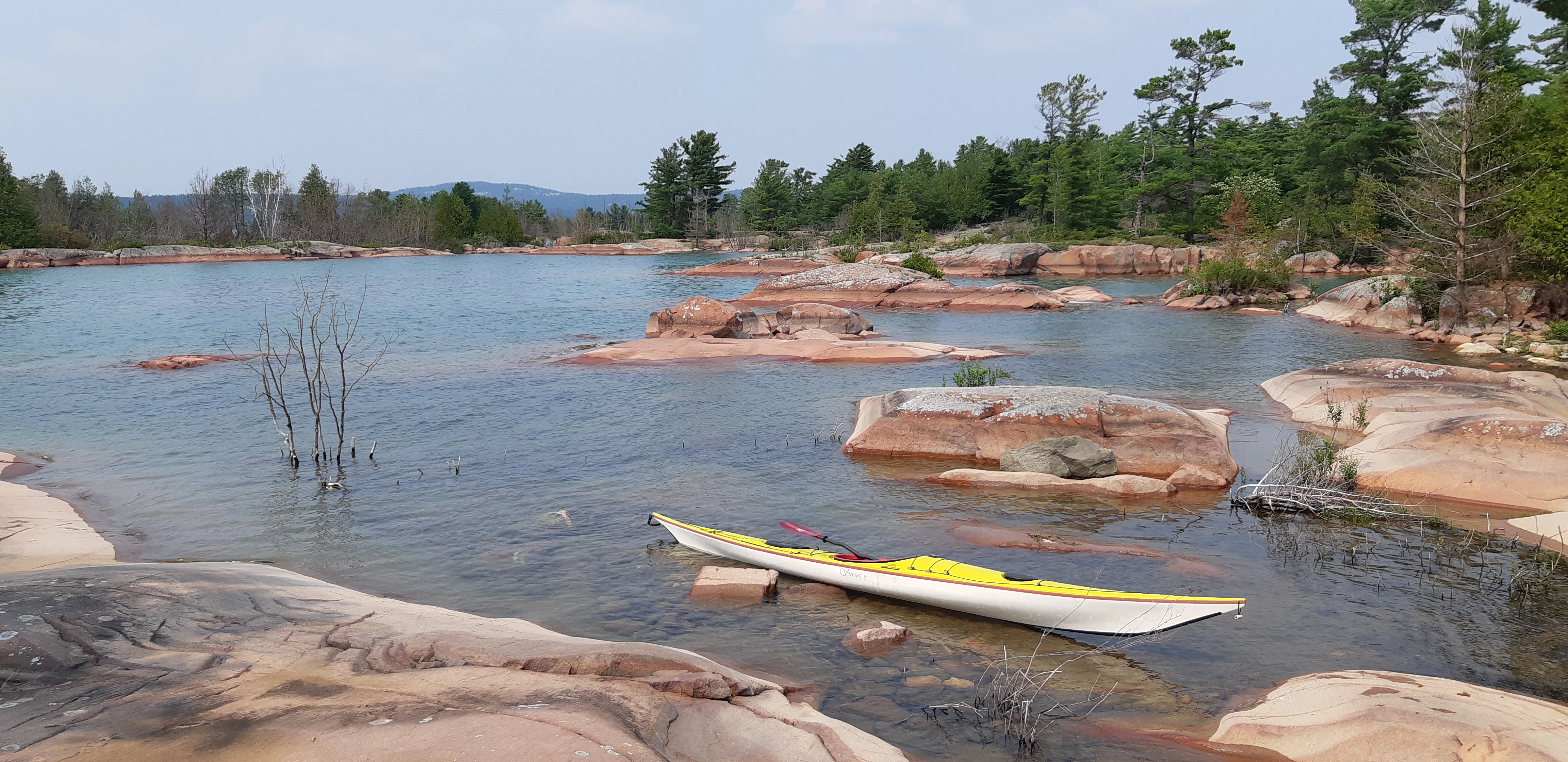 George Island across from Killarney, Ontario, with a sea kayak next to a rock and the La Cloche Mountains far in the distance